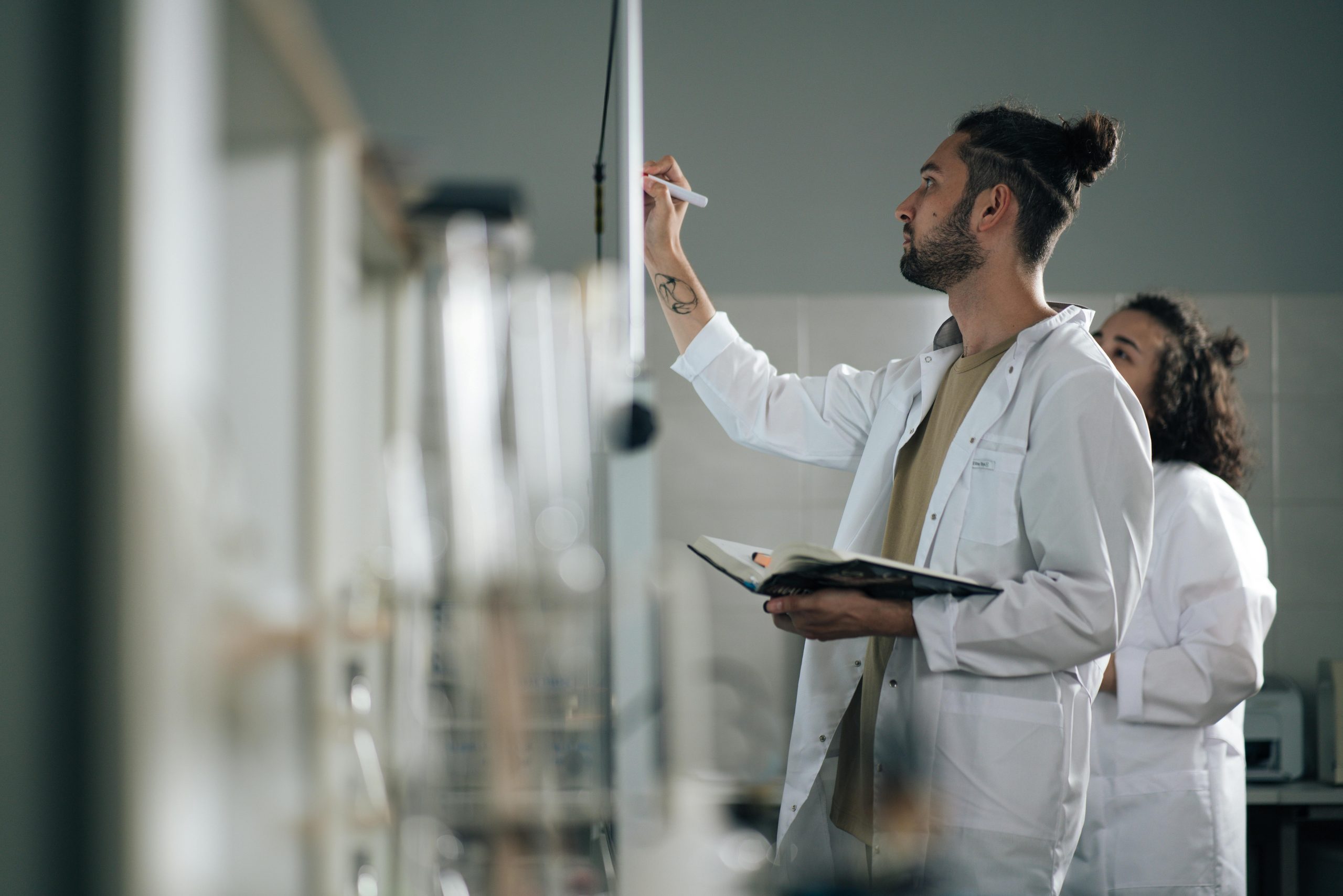 A scientist in a lab coat writing on a whiteboard in a modern laboratory setting.